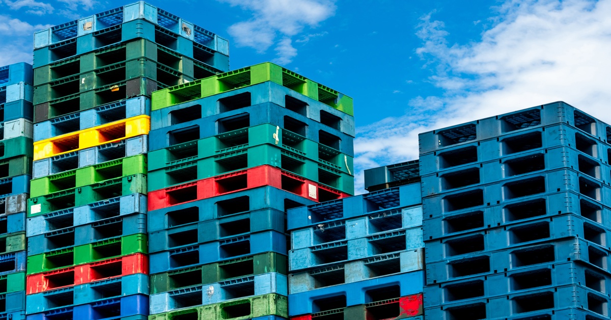 Closeup of several plastic shipping pallets in various colors all stacked together in rows with the sky in the background.